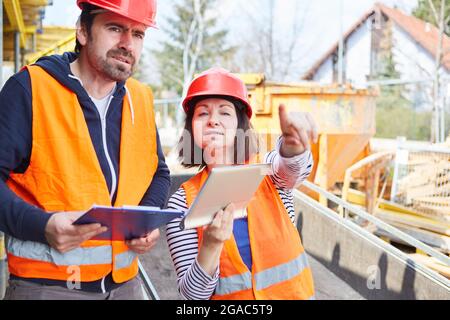 Lavoratore e architetto che utilizzano insieme un computer tablet durante la pianificazione della costruzione in cantiere Foto Stock