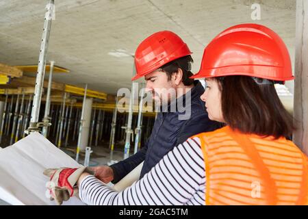 Artigiano e architetto con pianta durante la progettazione della costruzione nel guscio del cantiere della costruzione della casa Foto Stock