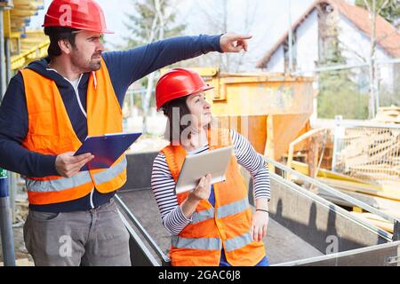 Caposquadra con lista di controllo e architetto con computer sul cantiere progettazione di un progetto di costruzione Foto Stock