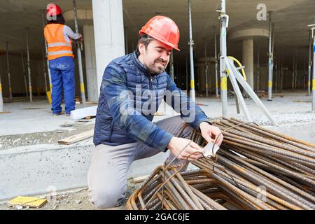 Lavoratori edili durante il controllo di qualità della fornitura di acciaio di rinforzo sul guscio di un cantiere Foto Stock