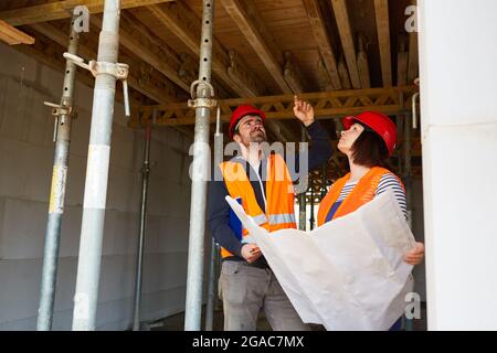 Caposquadra artigiano e architetto con piano di costruzione discutono la ristrutturazione di un soffitto sul cantiere Foto Stock