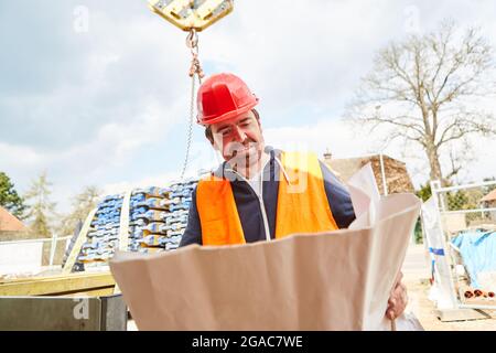 Architetto o caposquadra con progetto sul cantiere con consegna di legname sullo sfondo Foto Stock