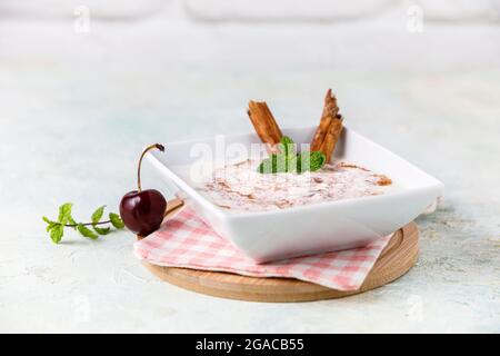 Budino di riso fatto in casa con cannella e ciliegie in una ciotola bianca su legno Foto Stock
