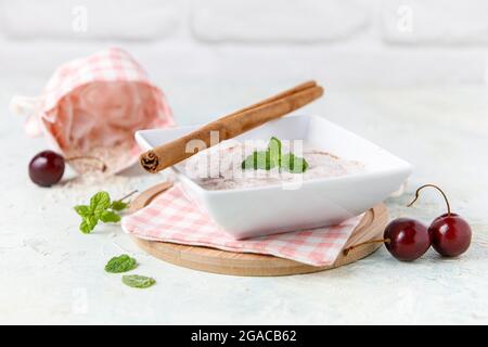 Budino di riso fatto in casa con cannella e ciliegie in una ciotola bianca su legno Foto Stock