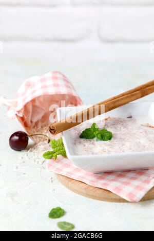 Budino di riso fatto in casa con cannella e ciliegie in una ciotola bianca su legno Foto Stock