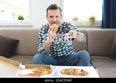 Uomo che guarda la TV mentre si mangia la pizza. Trascorrere del tempo libero a casa Foto Stock