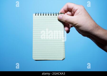 un blocco note in una mano dell'uomo con sfondo blu Foto Stock