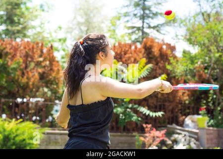 Bambina che gioca a tennis nel suo giardino in una giornata estiva. Focus Girl selettivo Foto Stock