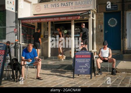 Persone che controllano il proprio telefono mentre attendono il cibo da portare via alla St Ives Bakery al porto di St Ives, Cornovaglia, Regno Unito. Foto Stock