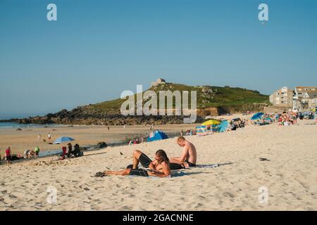 Due giovani si sedettero a leggere sull'estate di Porthmeor Beachin. St Ives, Cornovaglia, Regno Unito. Foto Stock