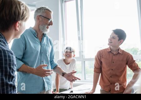 sorridente insegnante che gesturing mentre parla con gli allievi multietnici in classe Foto Stock
