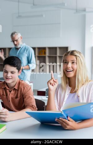 Ragazzino sorridente che ha idea e tiene il libro in classe Foto Stock