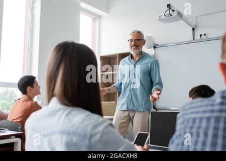 un insegnante che gesturing positivo mentre parla vicino agli adolescenti durante la lezione a scuola Foto Stock