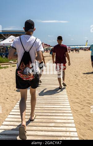 Sozopol. Burgas Bulgaria - 07 24 2021: Uomini in pantaloncini da spiaggia e t-shirt che camminano su una passerella durante una soleggiata giornata estiva. Il mare si può vedere nella Foto Stock