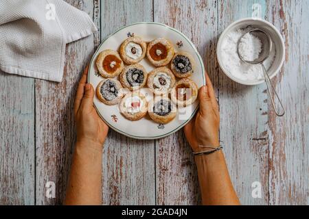 Mani femminili che tengono piatto rustico con torta appena fatta in casa farcito con formaggio cremoso, marmellata, papavero. Biscotti pronti per mangiare su un tavolo di legno. Delizioso Foto Stock