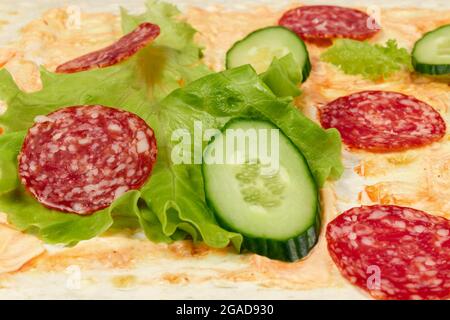 le verdure fresche a fette giacciono su pane pita sottile con ketchup e salsa maionese. salsiccia di salame, cetriolo e lattuga. primo piano Foto Stock