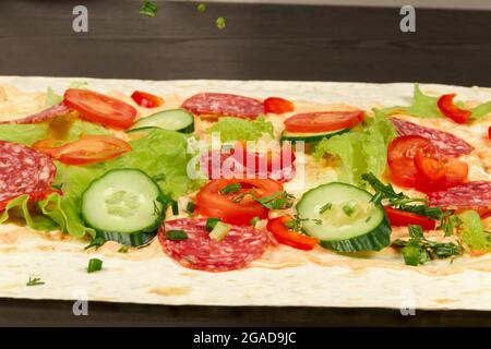 gli ingredienti per lo shawarma sono disposti su un pita sottile: pomodori, verdi, salumi, formaggi, cetrioli e lattuga da vicino Foto Stock