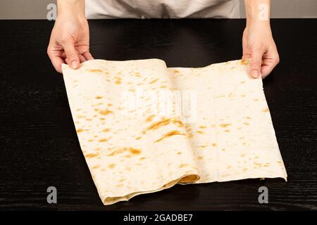 le mani femminili stendono il pane fresco della pita per fare lo shawarma sullo sfondo di un tavolo di legno nero primo piano Foto Stock