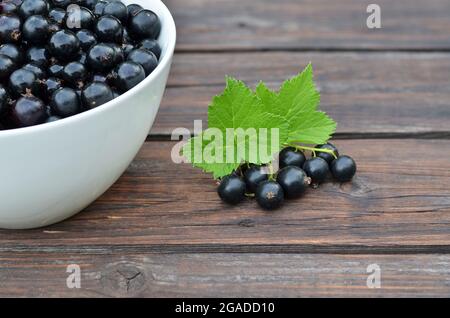 Bacche mature di ribes nero con foglie verdi su un vecchio tavolo di legno. Concetto di alimentazione sana. Foto Stock