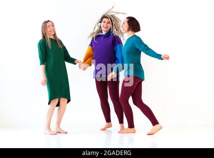 Immagine di tre allegre e giocose donne a piedi nudi di diversa età che tengono insieme le mani, saltando e divertendosi, godendo la vacanza, celebrando i realizzemen Foto Stock