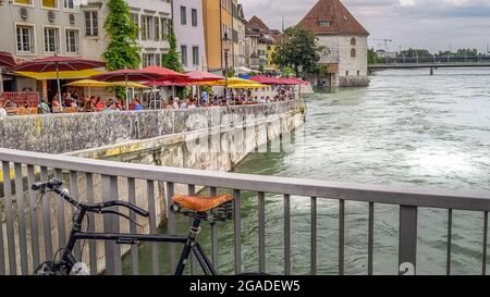 Aperitivo rilassante nei bar sotto gli ombrelloni lungo il fiume di in Soletta. Vista dal ponte sul fiume Aare con una bicicletta d'epoca parcheggiata Foto Stock