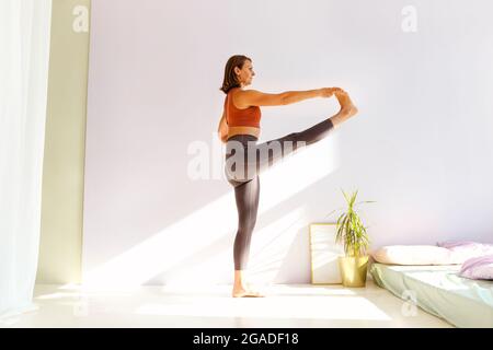 Sportivo di mezza età bella donna bruna pratica yoga, facendo esercizi di stretching mentre in piedi in posizione estesa mano-a-piedi, outthita ha Foto Stock
