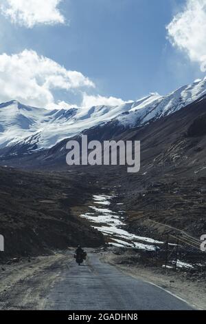 Guida turistica di una moto d'avventura su una strada dura e accidentata sulla montagna rocciosa in un tramonto. Foto Stock