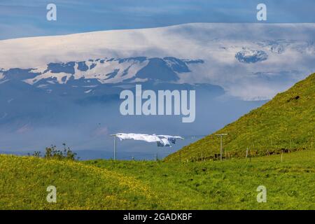 forti venti islandesi soffiano il lavaggio asciutto sulla linea uno la collina sopra la spiaggia di reynisfjoru con il ghiacciaio miralsjokull dietro Foto Stock