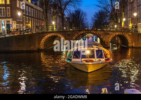 Crociera turistica in barca sui canali e ponte con archi, illuminati di notte, canali Herengracht e Leidsegracht, Amsterdam Foto Stock