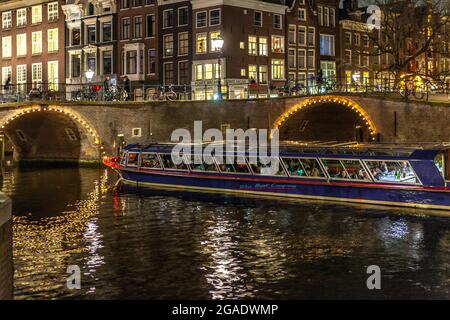 Crociera turistica in barca sul canale e ponte con archi, illuminati di notte, canali Herengracht e Reguliersgracht, Amsterdam Foto Stock