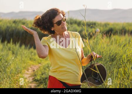 Una donna allegra e vitale, nei suoi anni '70, regola i capelli dopo aver rimosso il cappello durante una passeggiata in una zona naturale, Spagna Foto Stock