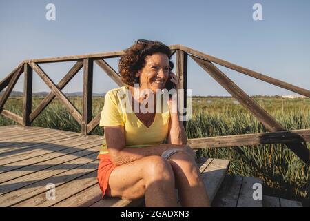 Una donna allegra e vitale, negli anni '70, che chiacchiera animatamente al telefono, da una zona naturale vicino al Mar Mediterraneo, in Spagna Foto Stock
