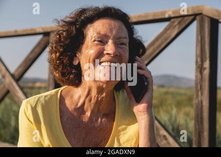 Una donna allegra e vitale, negli anni '70, che chiacchiera animatamente al telefono, da una zona naturale vicino al Mar Mediterraneo, in Spagna Foto Stock