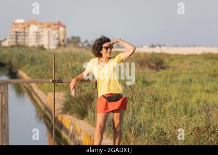 Una donna allegra e vitale, nei suoi anni '70, osserva il paesaggio intorno a lei, accanto ad una spiaggia naturale, al tramonto, nel Mar Mediterraneo, in Spagna Foto Stock