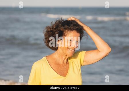 Una donna allegra e vitale, nei suoi anni '70, cammina su una spiaggia al tramonto, sulle rive del Mar Mediterraneo, Spagna Foto Stock