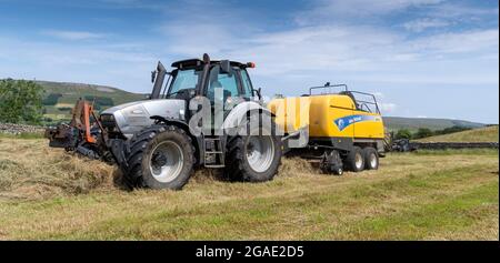 Appaltatore con una pressa argento Hurlimann e New Holland, che fa grandi balle quadrate di fieno in un prato di dales tradizionale, Hawes, North Yorkshire, Regno Unito. Foto Stock