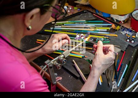Artista di vetrai che forma il vetro caldo di murano in una statuina sotto un getto di gas caldo da un bruciatore a gas. Fine art. Fatta a mano fuoco selettivo. Foto Stock