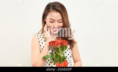 Bella ragazza tenera tiene le rose rosse nelle sue mani e guarda attentamente di lato. Foto su sfondo bianco. Foto Stock