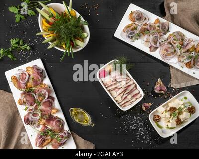 Patate al forno con pesce, pancia di maiale a fette, formaggio e verdure sul tavolo Foto Stock