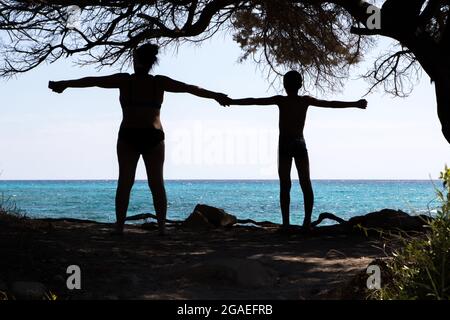 Silhouette di due persone con un mare cristallino sullo sfondo vicino alla spiaggia di Cala Liberotto, Sardegna. Foto Stock