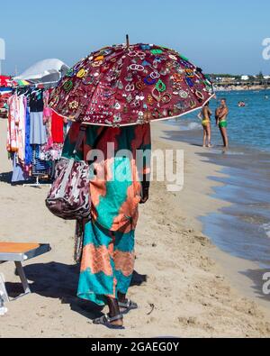 B, INDONESIA - 15 maggio 2019: Una donna in abiti tradizionali e un ombrello colorato mentre si cammina sulla spiaggia di Bali, Indonesia Foto Stock