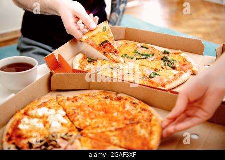 Primo piano le mani della gente che prende le fette di pizza dalla scatola della pizza. Amici che mangiano la pizza insieme. Consegna di cibo. Cucina italiana. Foto Stock