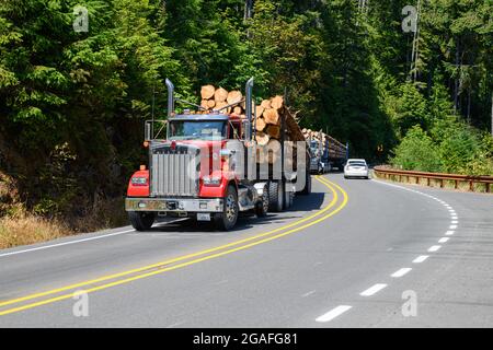 Lake Crescent, WA, USA - 27 luglio 2021; autocarri per tronchi caricati che viaggiano lungo le curve dell'autostrada 101 lungo il lago Crescent nello stato di Washington Foto Stock