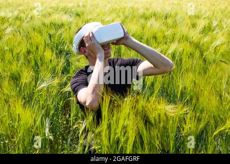 Uomo che usa occhiali di realtà virtuale all'esterno in natura su un campo di coltivazione del grano. Foto Stock