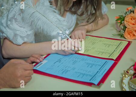 Sposo e sposa registrano il matrimonio. Donna mette la sua firma sul matrimonio . La mano di una donna firma e registra il suo matrimonio con la donna che ama Foto Stock