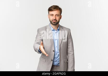 Ritratto di uomo d'affari sicuro con barba, vestito grigio, mano che si estende per la stretta di mano, saluto, presentarsi, in piedi su bianco Foto Stock