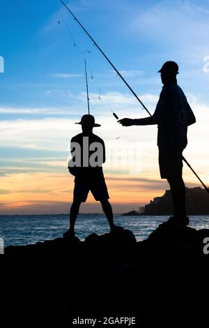 Salvador, Bahia, Brasile - 25 aprile 2021: Silhueta de pescadores com suas varas de pesca sobre as rocas em busca de peixes. Foto Stock