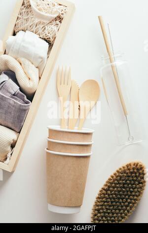 Stoviglie di cartone monouso eco-friendly, bottiglia d'acqua di vetro, spazzola per il corpo, borse per la spesa in tessuto su sfondo bianco. Disposizione piatta, vista dall'alto Foto Stock