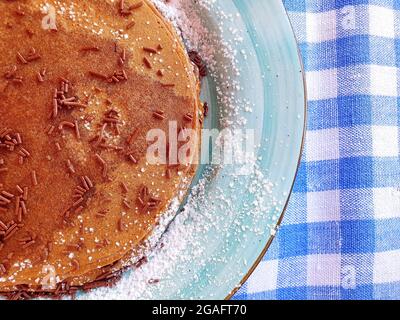 Frittelle di cioccolato su un piatto blu. Le frittelle sono cosparse di gocce di cioccolato e zucchero in polvere. Foto Stock