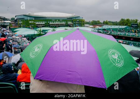 Gli spettatori si accoccolano sotto gli ombrelli sulla Corte 12 durante i Campionati di Wimbledon 2021 Foto Stock